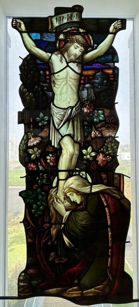 Centre window of the Rosary Chapel Bundoran with a fragment of a stained glass window created c. 1899 by Joshua Clarke & Sons, Dublin, depicting Mary Magdalene kneeling at the feet of Jesus Christ at the cross. This Window and Plaque is in Memory of the 10 People who lost their lives in the Central Hotel Fire Bundoran on 8th August 1980.